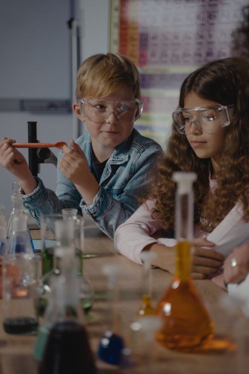 Free Two children in protective goggles conducting a chemistry experiment with colorful liquids in a classroom. Stock Photo