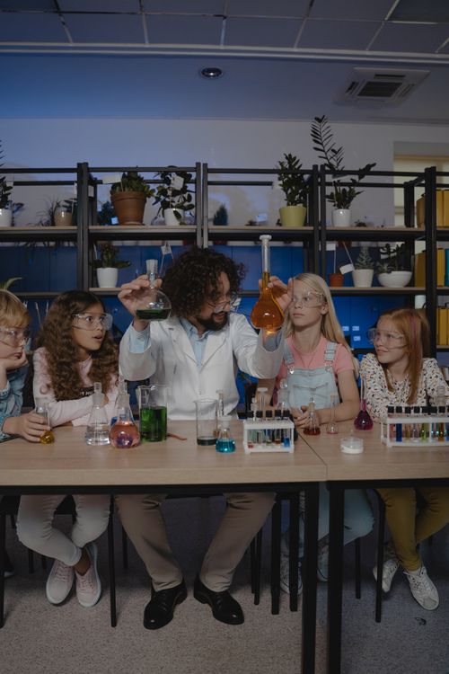 Free Teacher demonstrating chemistry experiment to engaged students with diverse backgrounds in a classroom setting. Stock Photo