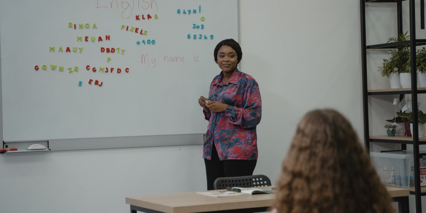 A teacher explaining English concepts to a student in a classroom setting with a whiteboard.