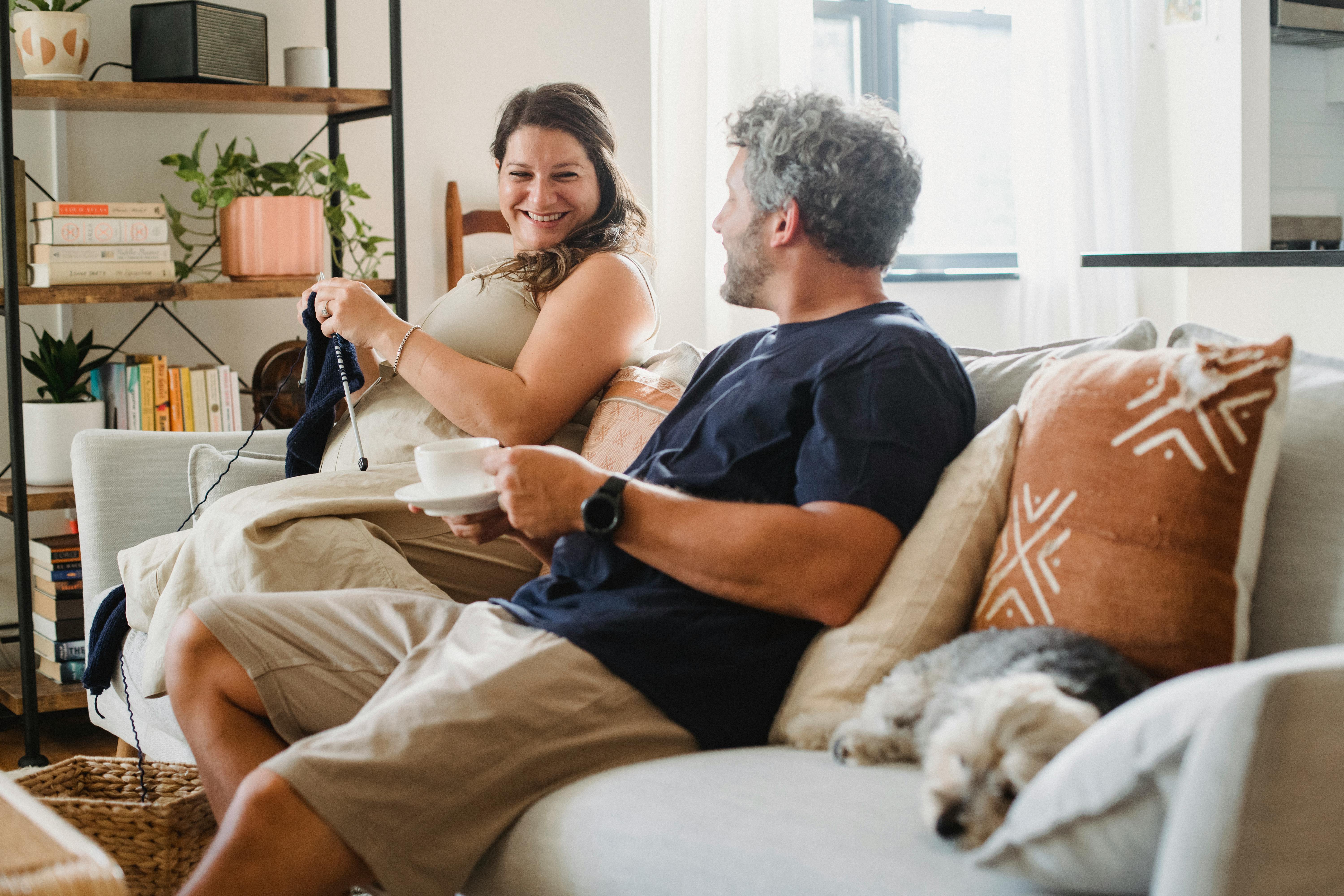 positive woman knitting and looking at husband having coffee