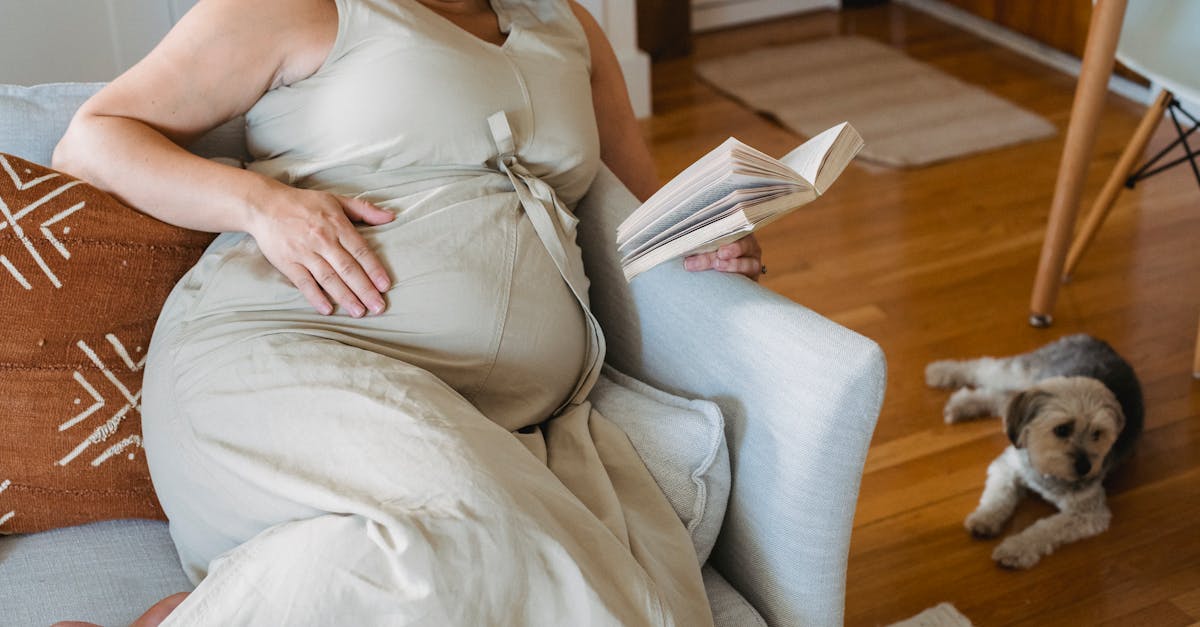 Crop positive woman reading book while resting on couch with dog