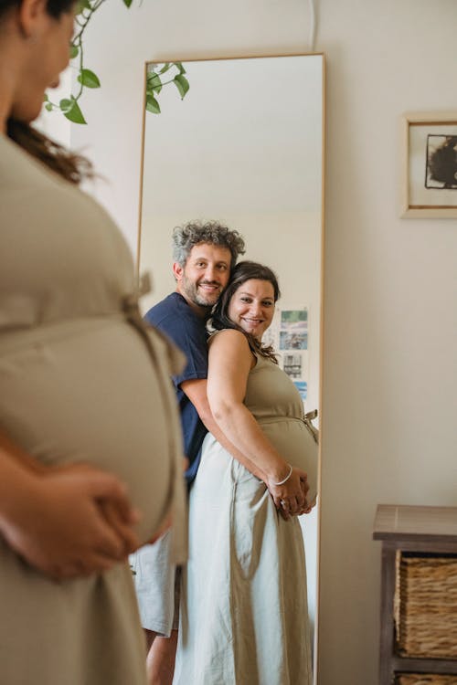 Cheerful couple touching pregnant tummy and looking in mirror