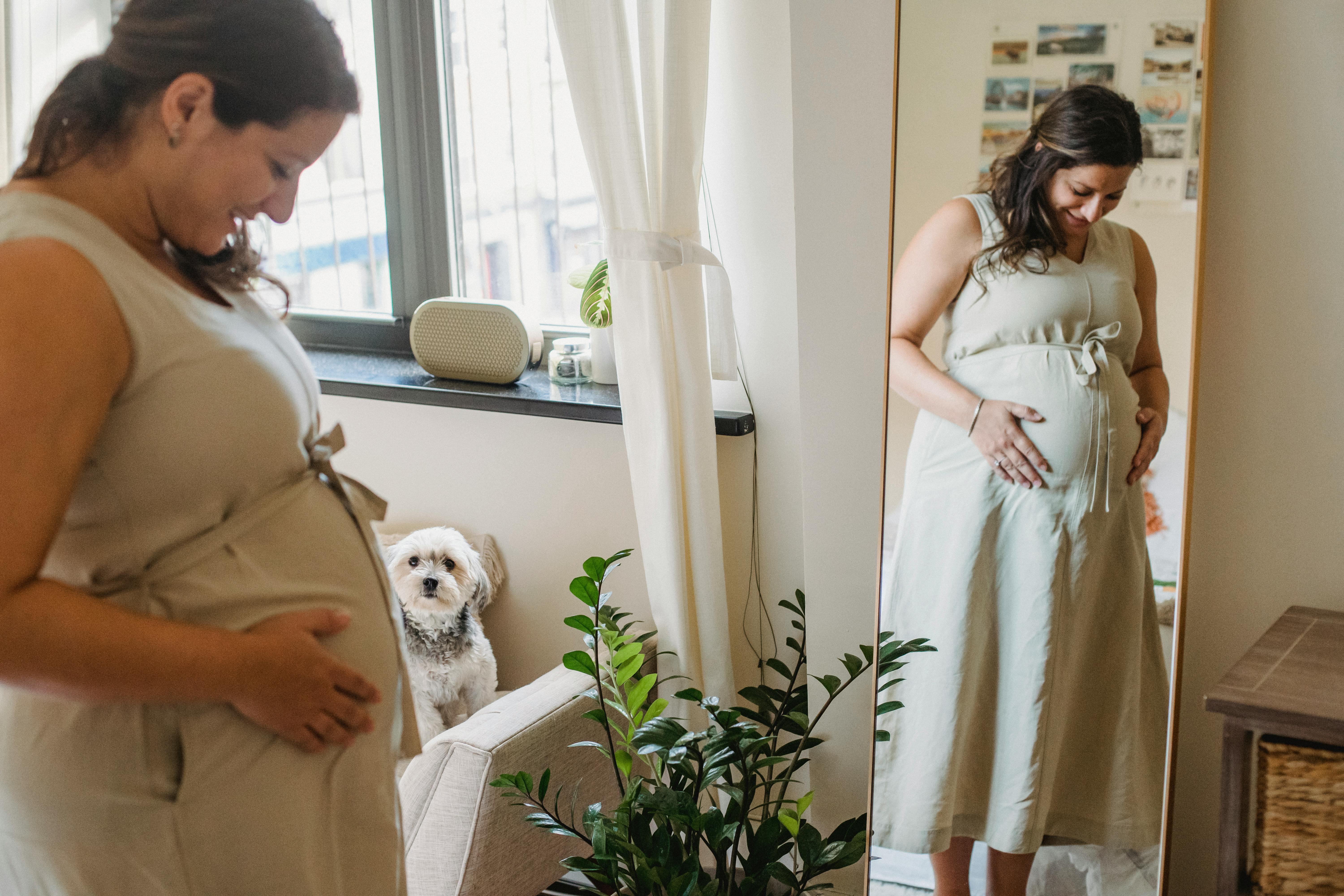 cheerful young pregnant woman touching belly near mirror