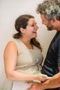 Side view of cheerful adult pregnant couple laughing and looking at each other while touching tummy against white background