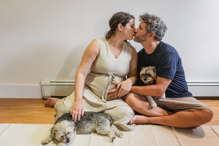 An affectionate couple embracing with their dogs, celebrating pregnancy in an indoor setting.