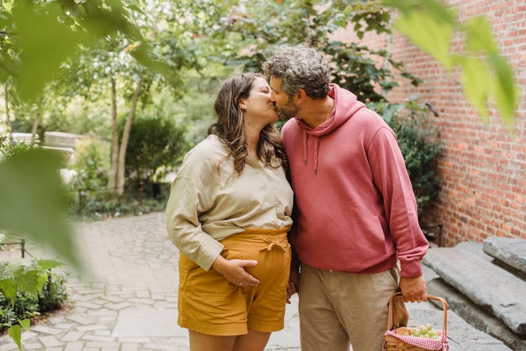 Content Man And Pregnant Woman Kissing In Yard Of Village House