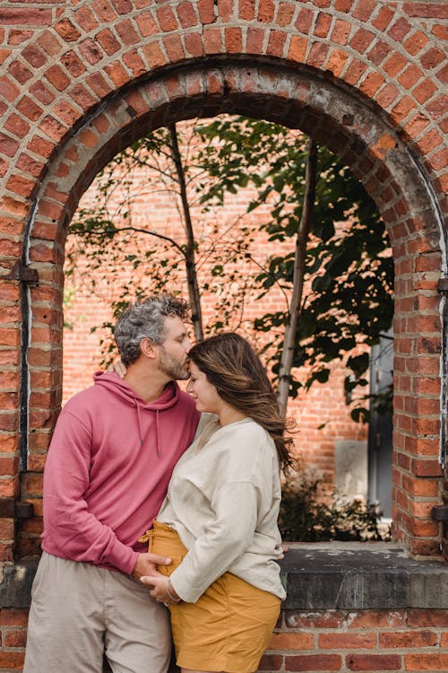 Man kissing forehead of pregnant wife in old house yard