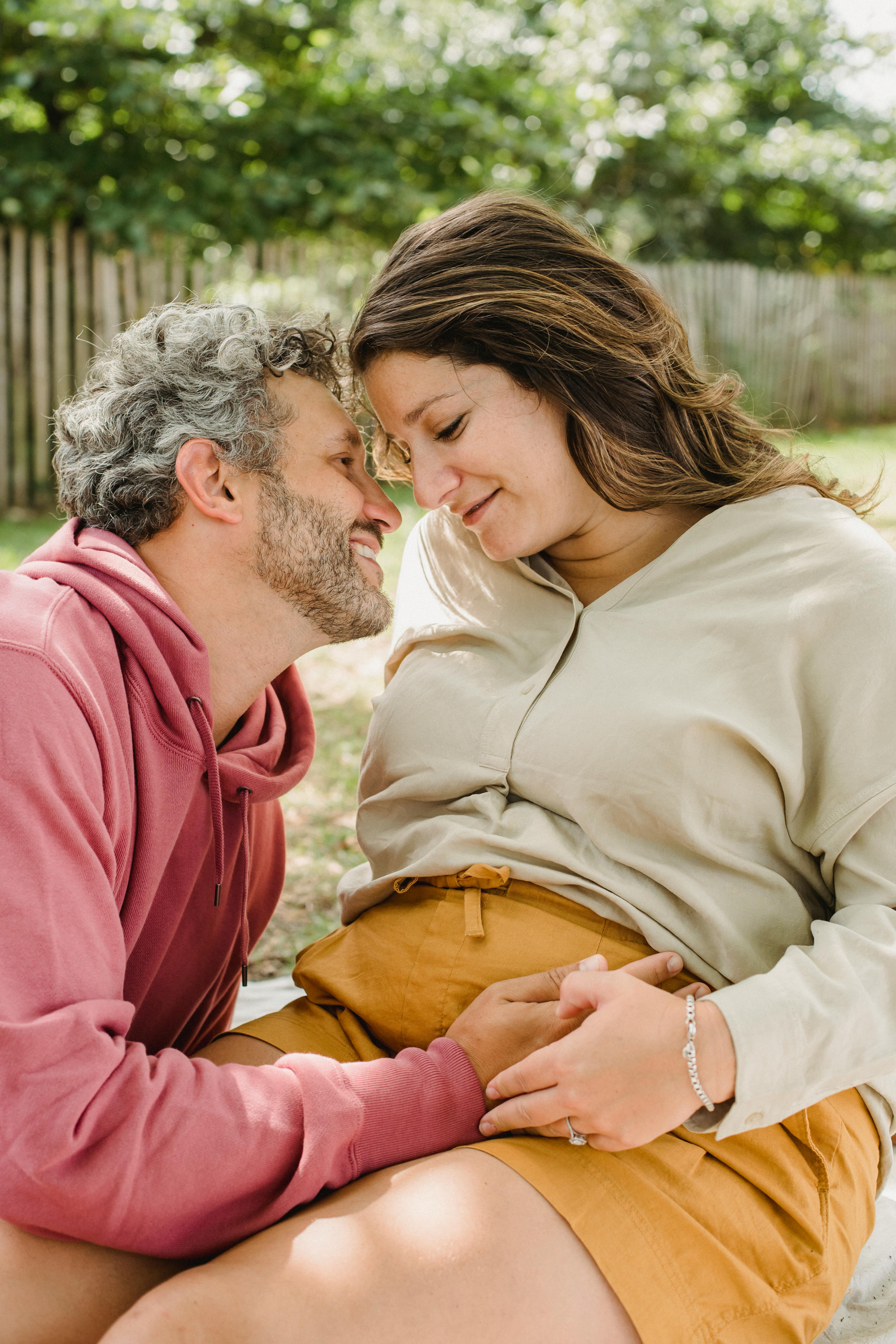 romantic pregnant spouses cuddling on lawn in park