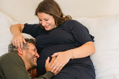 Laughing pregnant couple lying together on bed and having fun