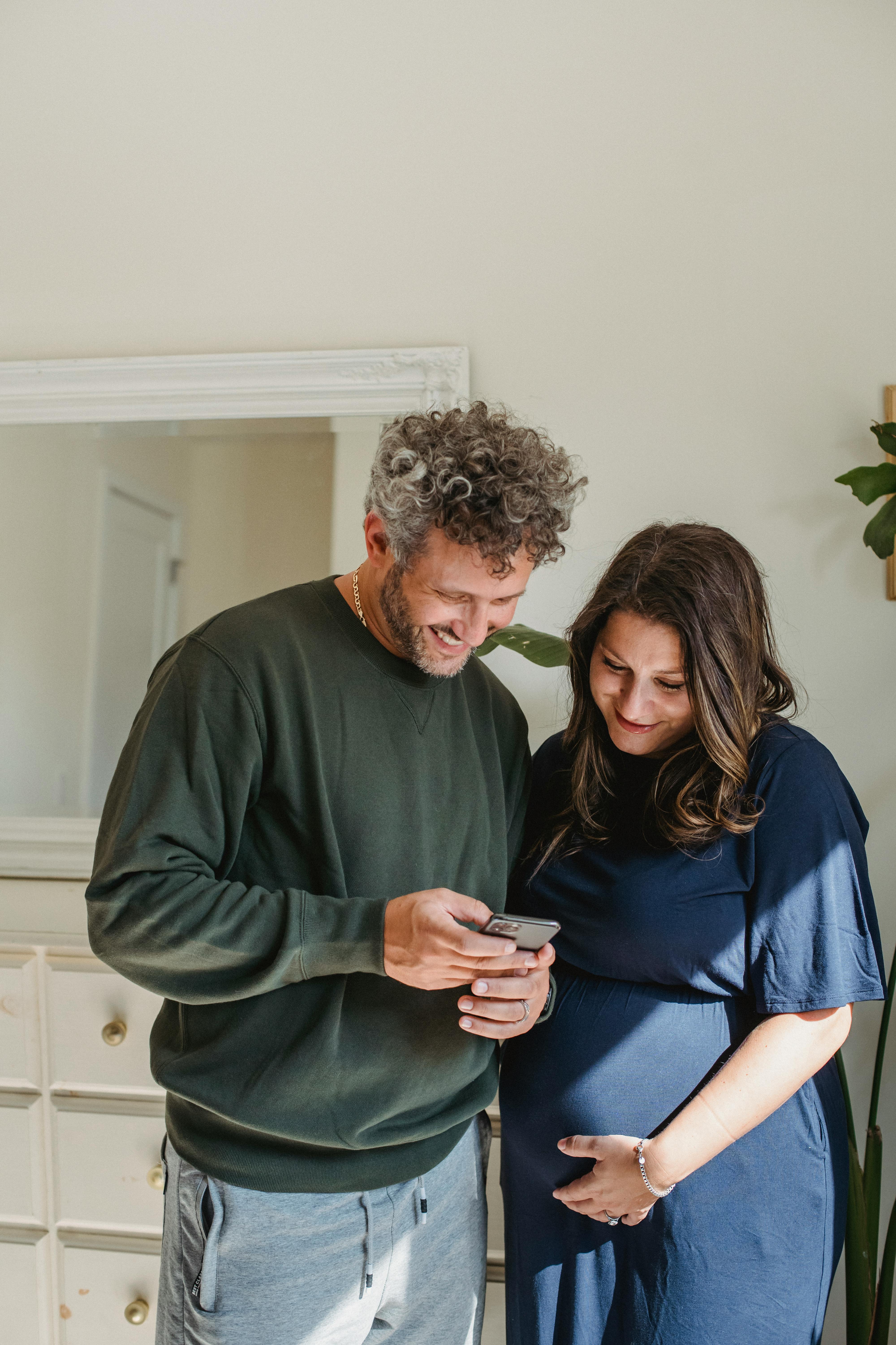 happy pregnant couple sharing smartphone at home