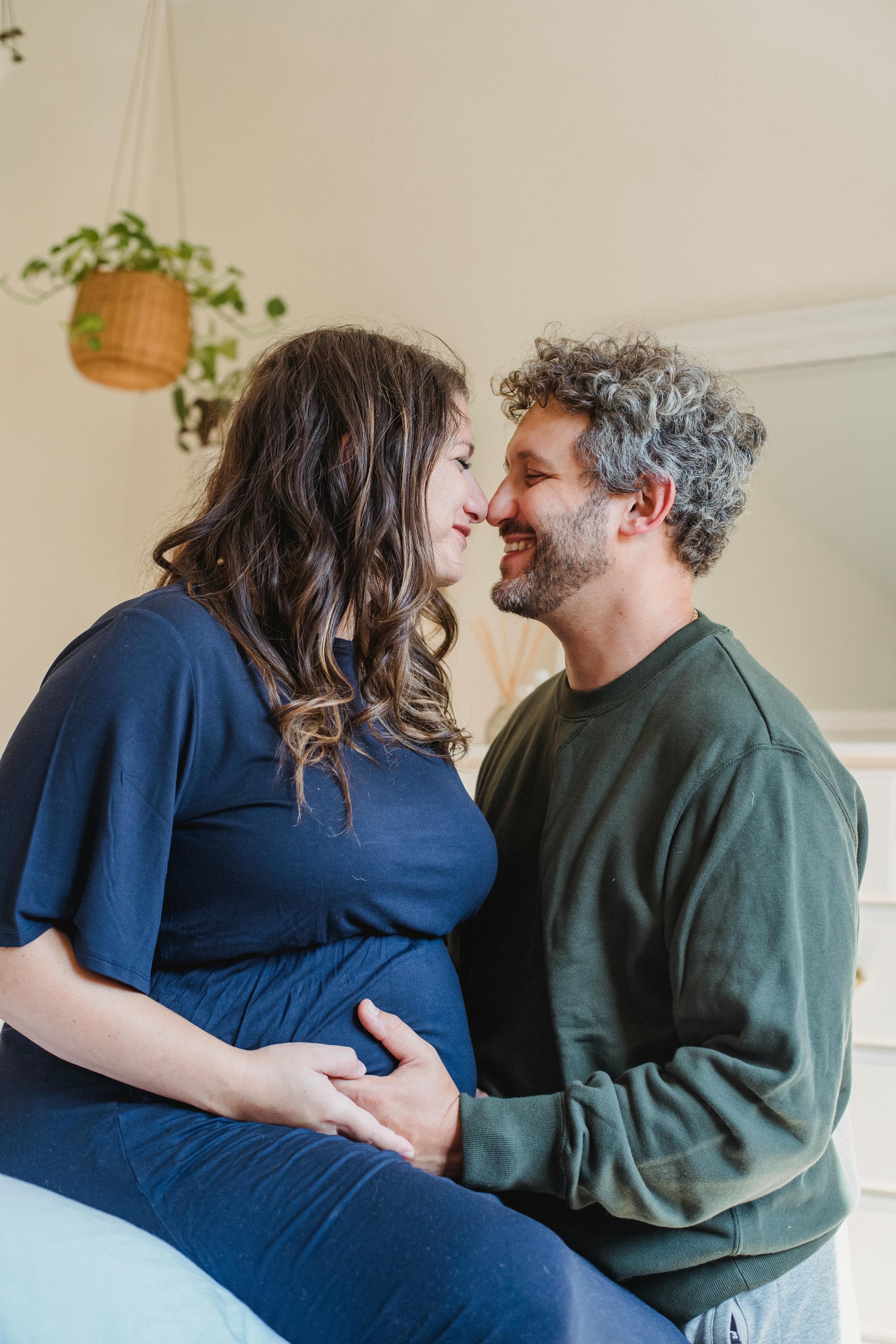 enamored pregnant couple embracing in bedroom in daylight