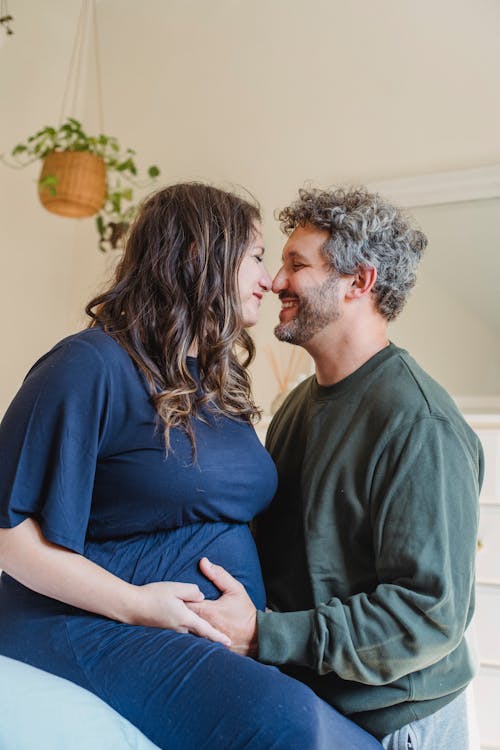 Enamored pregnant couple embracing in bedroom in daylight