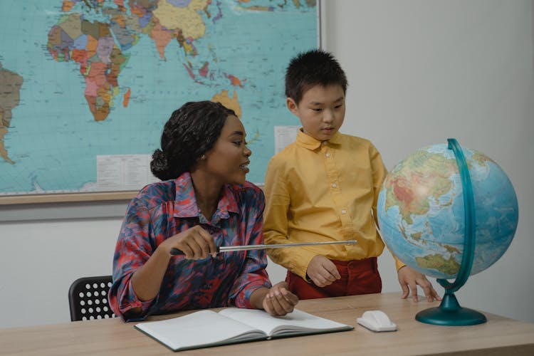 Teacher Pointing At A Globe Using A Pointer