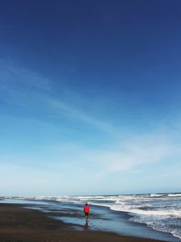 在广阔的蓝天下，一个人沿着宁静的海滩散步，给人一种放松和夏日的气息