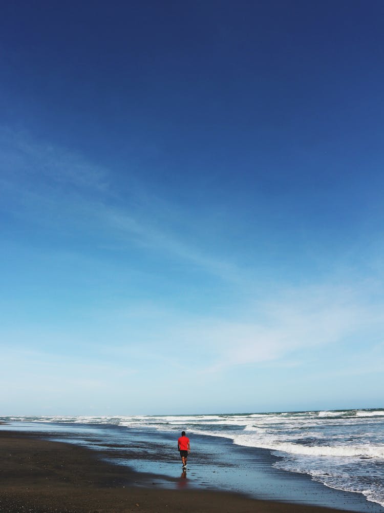 Man Walking On A Beach Alone In Distance 