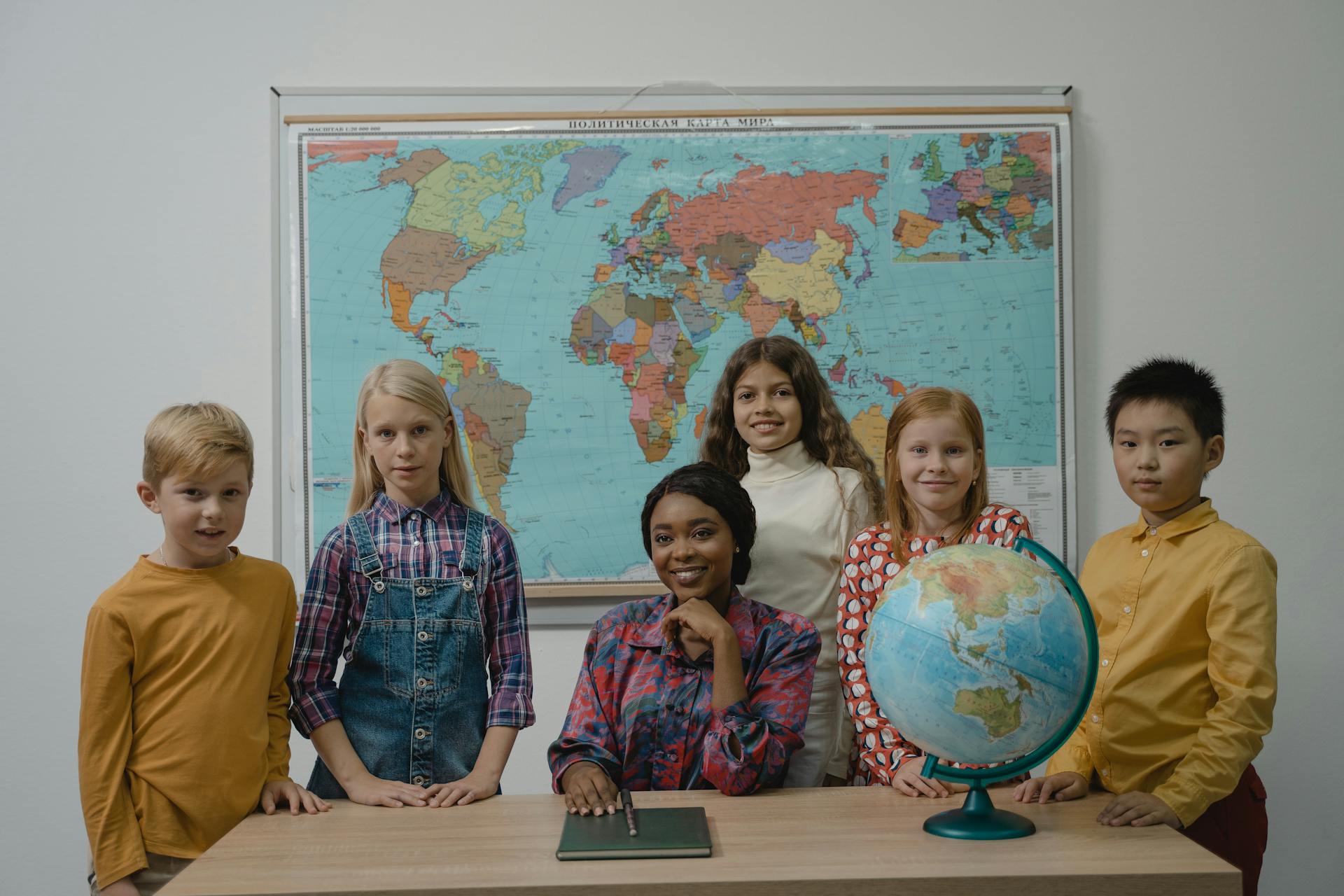 A diverse group of students with a teacher in a classroom setting featuring a globe and world map.