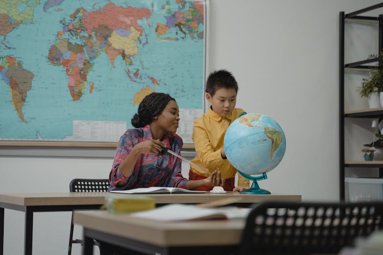 Teacher Teaching A Student About Geography Using A Globe