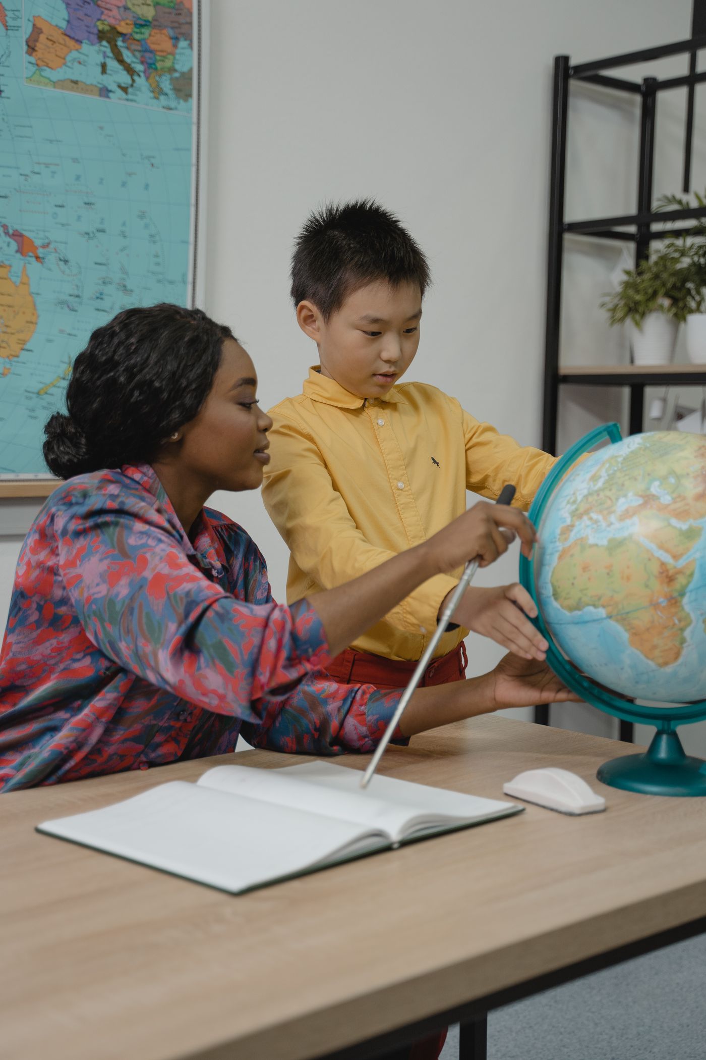 A female tutor guiding a primary-school student with a globe