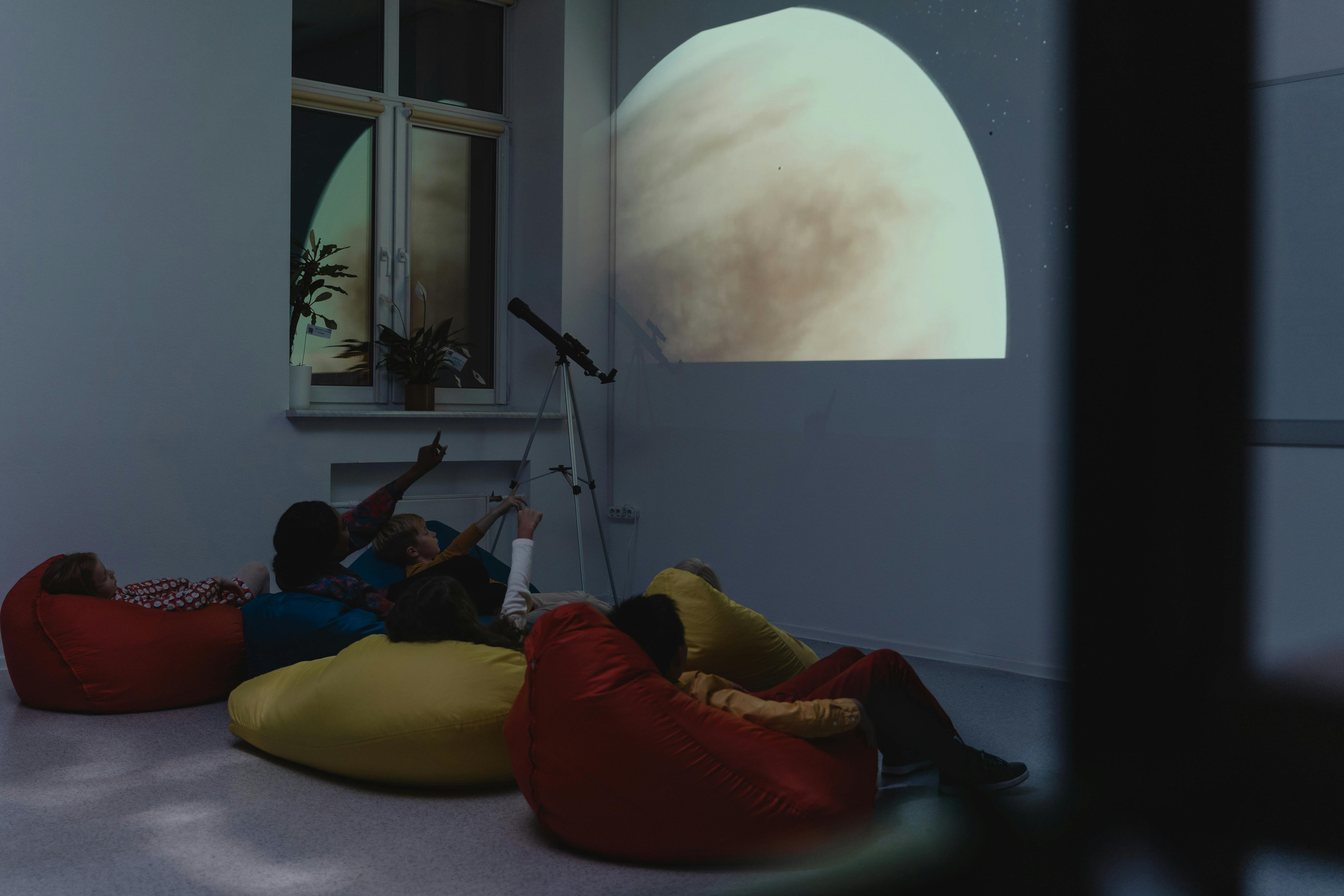 A group of kids learning astronomy with a telescope and projected planet image indoors.