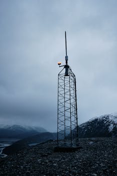 A solitary utility tower stands against a foggy snowy mountain backdrop, with a cool tone.