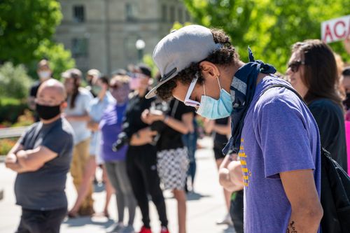 Free Side view of guy in casual clothes and cap and protective mask standing against crowd at sunny day Stock Photo