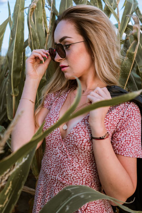 Young dreamy female in accessories and trendy wear with ornament looking away among greenery plants