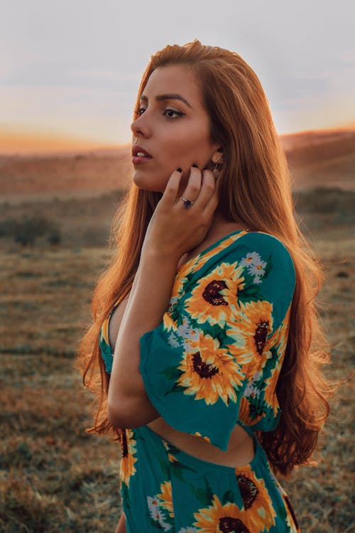 Pensive young woman resting on grassy hill in countryside at sundown