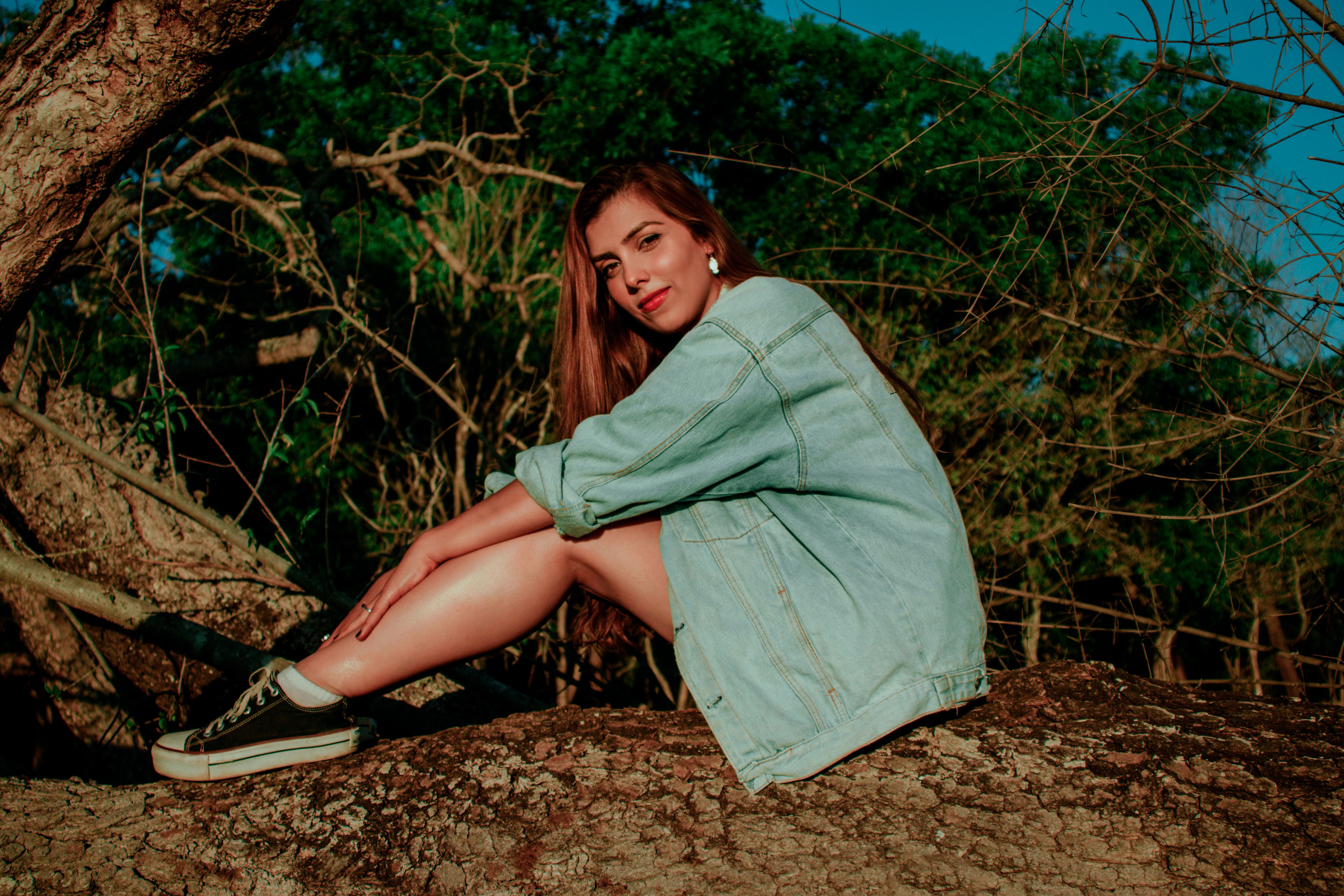 Relaxed young female sitting on tree trunk in woods under bright ...