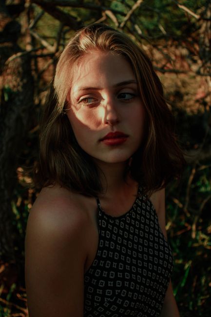 Thoughtful young female millennial in summer top relaxing in garden on sunny day and looking away dreamily