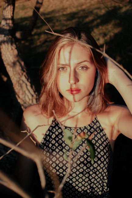 Confident young lady with ginger hair in summer top touching ginger hair and looking at camera while