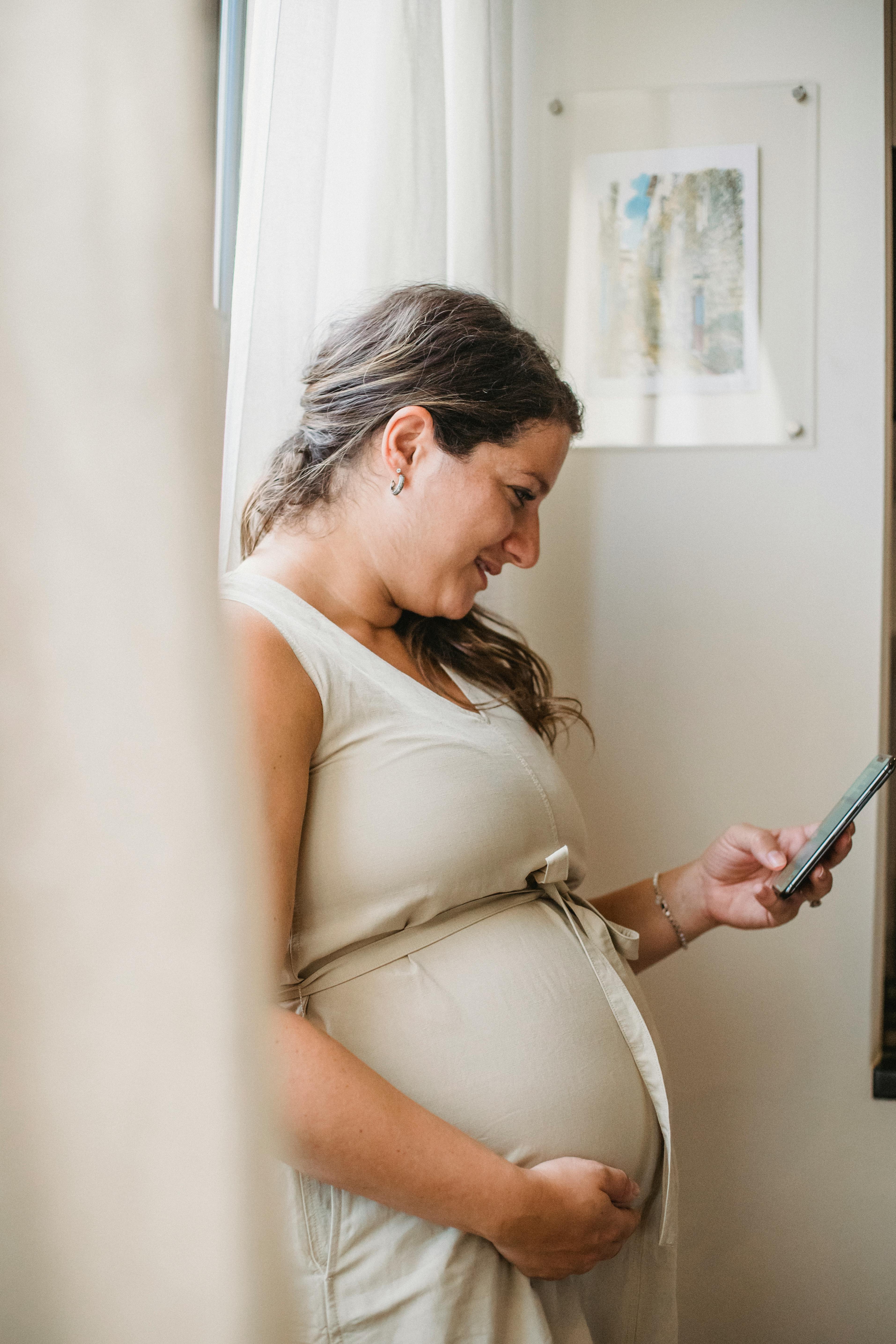 pregnant woman touching belly and using smartphone at home