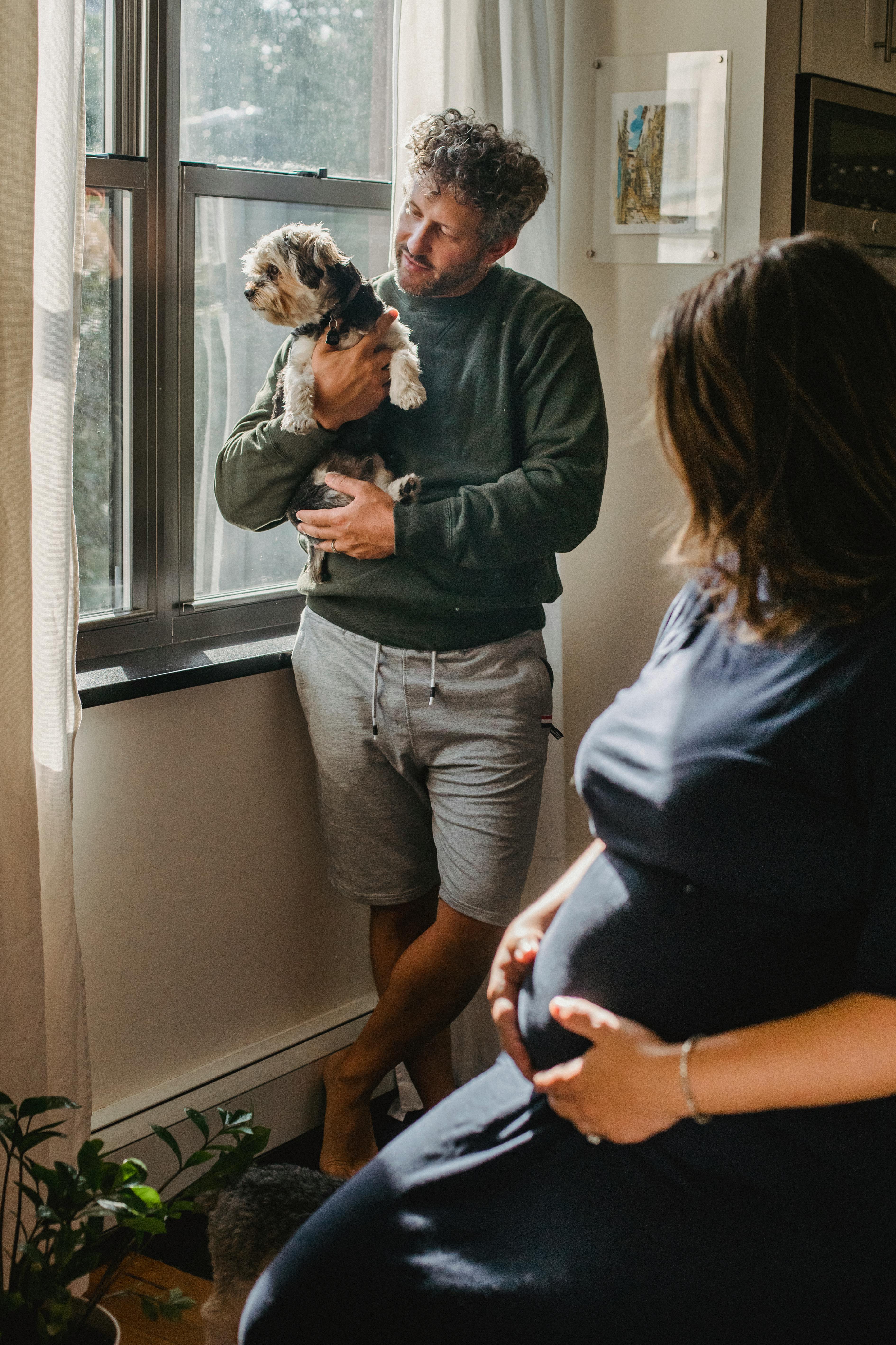 pregnant woman sitting near husband caressing adorable puppy