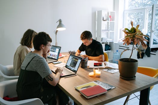 A group of young professionals collaborating in a modern office setting with laptops and documents.