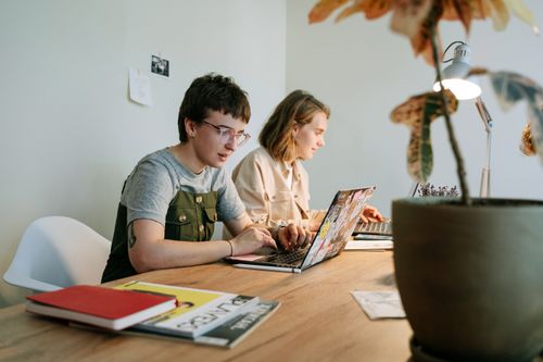 Free Two young professionals working collaboratively on laptops in a modern and creative workspace. Stock Photo