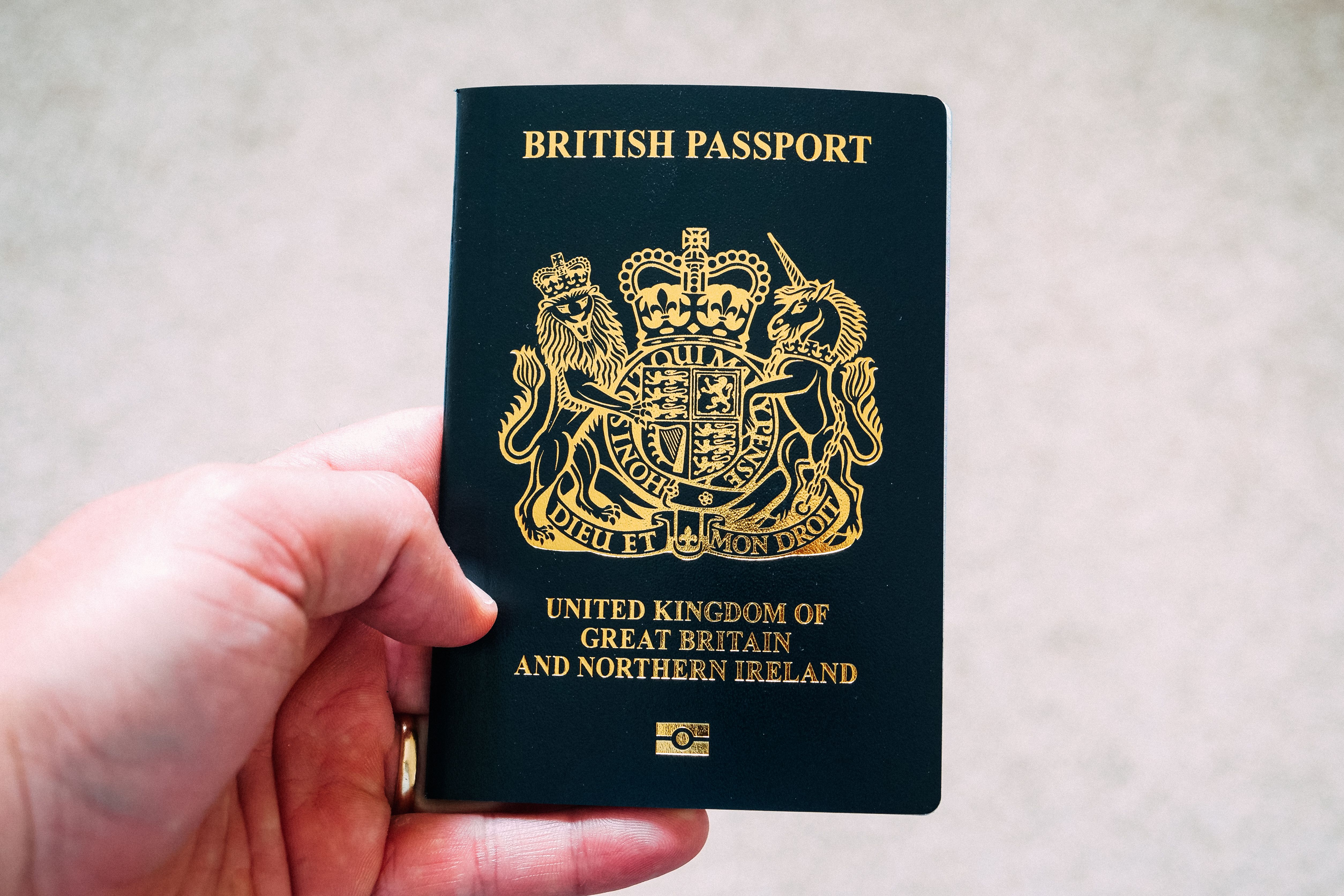 A hand holds a British passport displaying the United Kingdom coat of arms on the cover
