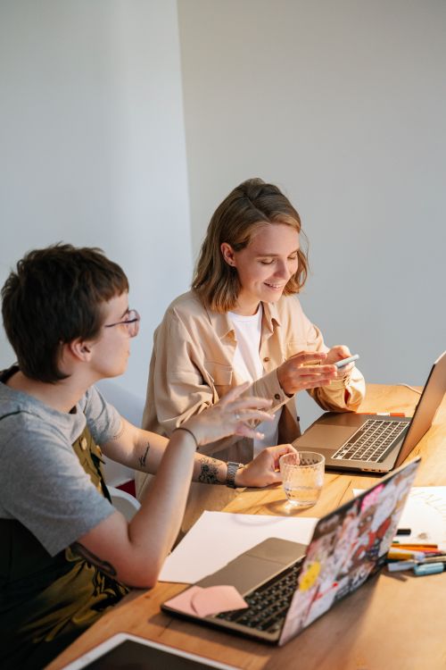Free Two young professionals brainstorming ideas at a collaborative workspace with laptops and notes. Stock Photo