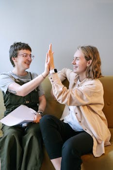 Two young professionals share a joyful high five in a casual office setting.