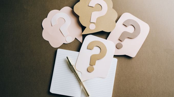 Des points d'interrogation en papier posés sur un cahier.