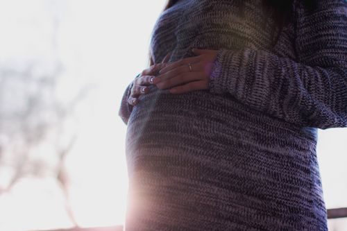Free Close-up of a pregnant woman in a cozy sweater gently holding her belly, symbolizing motherhood. Stock Photo