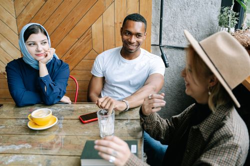 Free Three friends casually chatting and enjoying coffee at a cozy indoor cafe. Stock Photo