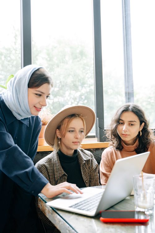 Free Three diverse women collaborating with a laptop in a bright, cozy workspace. Stock Photo