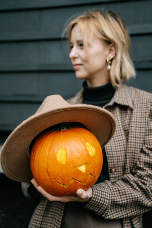 Free A woman holding a carved Halloween pumpkin wearing a hat, embracing the festive spirit. Stock Photo
