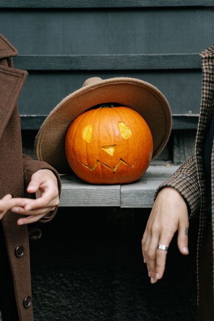 A carved pumpkin wearing a hat displayed on a ledge with two adults partially visible.
