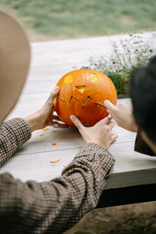 Free Two people carving a jack-o'-lantern on a wooden table outdoors during fall. Stock Photo