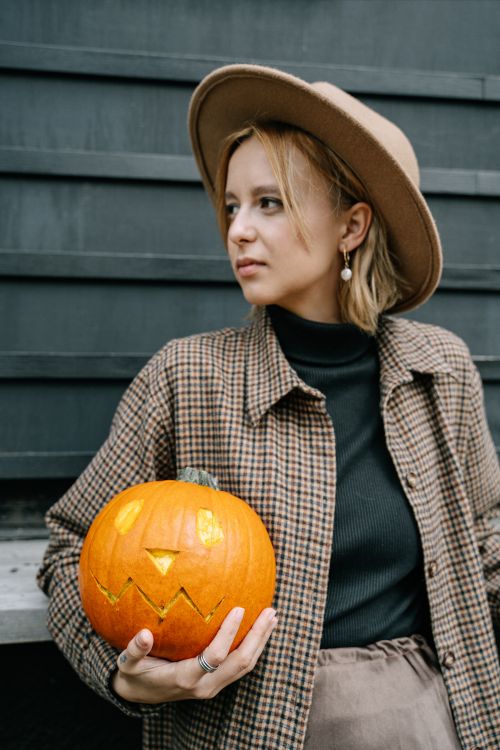 Free Woman in checkered coat holding a carved pumpkin for Halloween festivities. Stock Photo