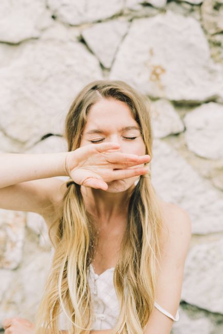 Woman with eyes closed and hand on face, standing against a stone wall.