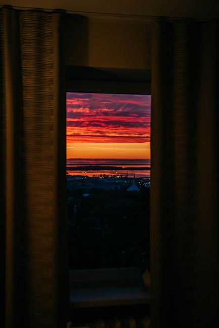 View through opened curtains near window at street with colorful cloudy sky at sunrise