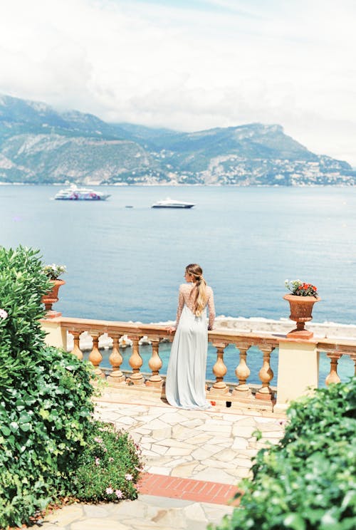 Woman in Long Light Blue Dress Standing Near Balusters