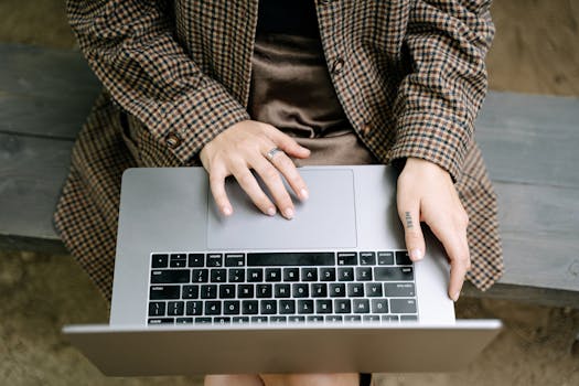 High angle view of individual using a laptop on a wooden bench while wearing a checkered coat.