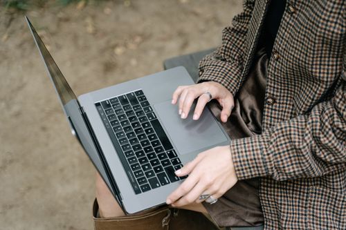 Free A woman typing on a laptop while sitting outdoors, showcasing remote work flexibility. Stock Photo